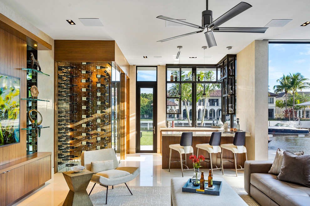 فضای نشیمن لوکس با ویترین شیشه‌ای نوشیدنی، بار مدرن با سه صندلی، پنجره‌های سرتاسری و چشم‌انداز به کانال آبی و ویلاهای مجاور