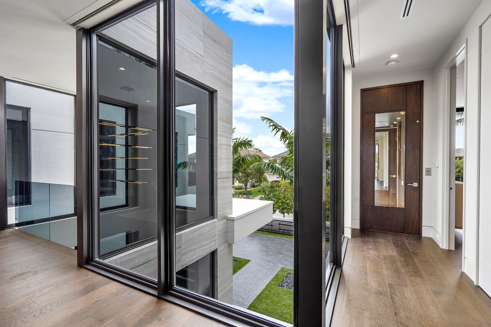 راهروی مدرن با پنجره‌های قدی مشرف به حیاط، کف‌پوش چوبی و ترکیب شیشه، چوب و بتن در معماری خانه معاصر.
