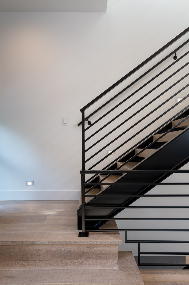 طراحی راه‌پله مدرن با ترکیب کف‌پوش چوبی، نرده فلزی مشکی و دیوار ساده سفید، تلفیقی از سادگی و زیبایی در معماری داخلی
