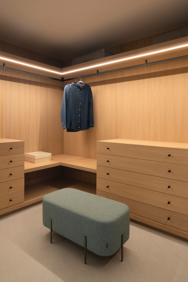 کلوزت مدرن با دیوارپوش و کشوهای تمام‌چوب روشن، نورپردازی خطی زیر سقف، نیمکت پارچه‌ای سبز خاکستری با پایه‌های مشکی، ریل مشکی لباس