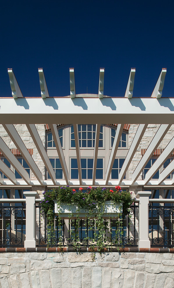 نمای پرگولای سفید با جزئیات گلدان‌های آویز، نرده فلزی مشکی و زمینه سنگی در معماری کلاسیک با پنجره‌های متعدد.