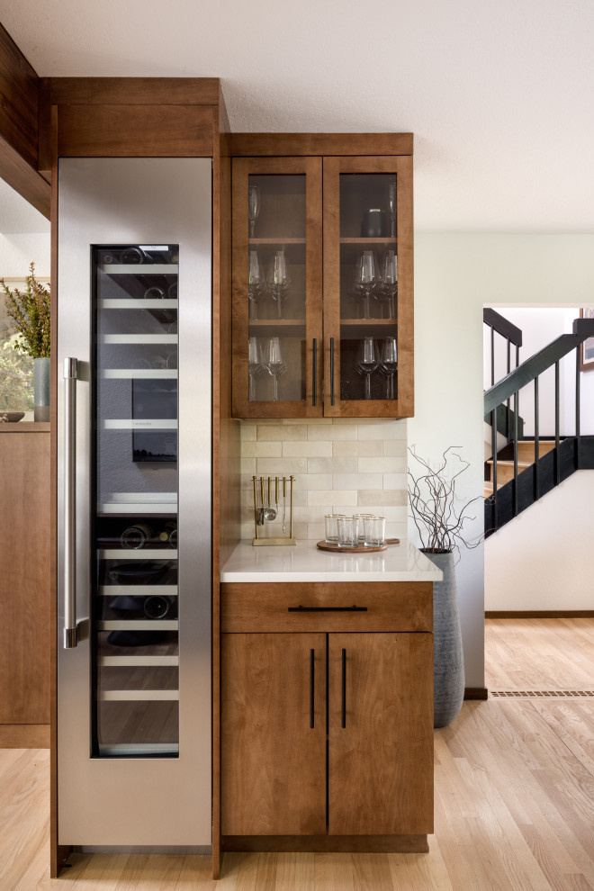  طراحی بار خانگی در آشپزخانه با کفپوش چوبی و کابینت‌های شیشه‌ای، همراه با کانترهای کوارتز سفید و بک‌اسپلش به رنگ بژ .