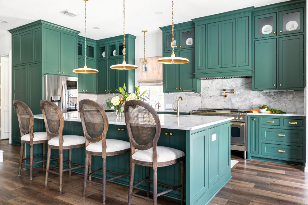 آشپزخانه سنتی و شیک با طراحی ال شکل، کفپوش لمینت قهوه‌ای، کابینت‌های سبز سبک شیکر، جزیره مرکزی و کاشی بین کابینتی مرمر خاکستری