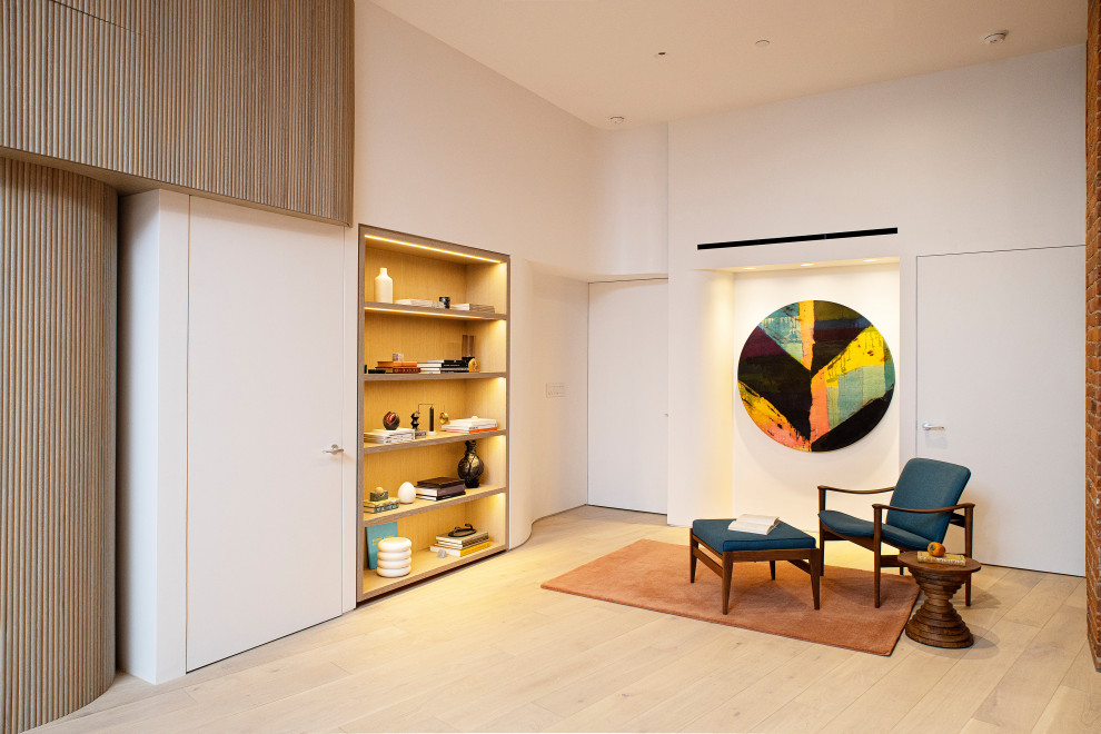  نشیمن مینیمال با صندلی راحتی آبی، کتابخانه دیواری مدرن و نورپردازی مخفی  - A minimalist living room with a blue lounge chair a modern wall-mounted bookshelf and concealed lighting.