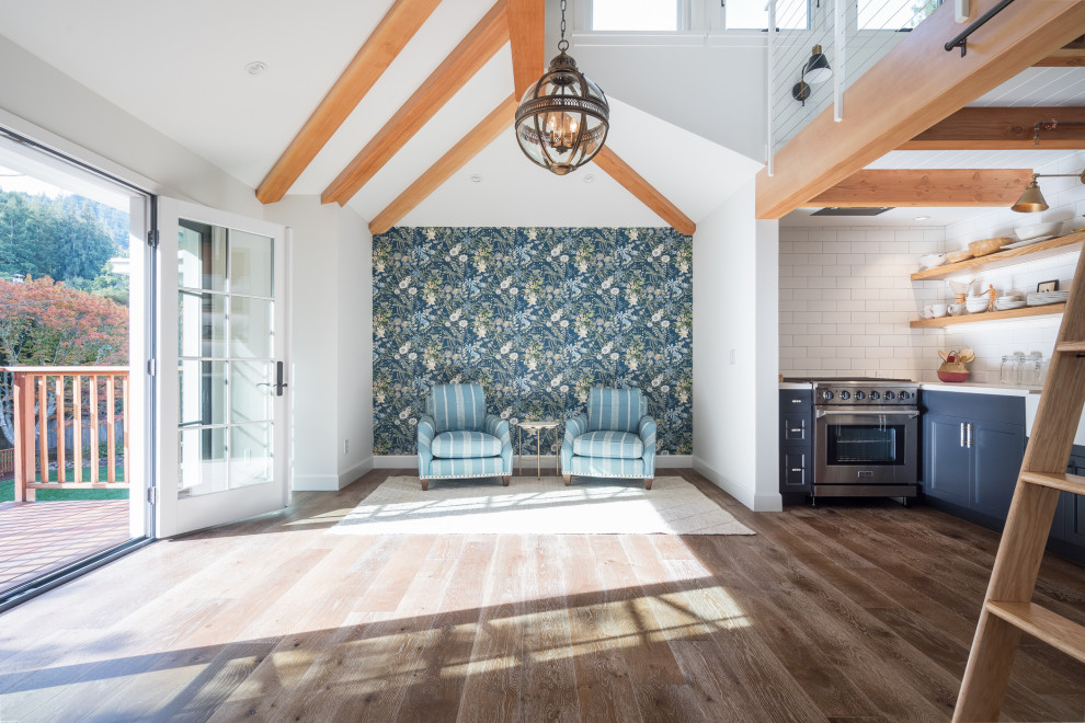 اتاق نشیمن شیک با طراحی باز و متوسط، کفپوش چوبی تیره، دیوارهای سفید، صندلی‌های راحتی راه‌راه آبی، دیوار شاخص با کاغذدیواری گل‌دار آبی.