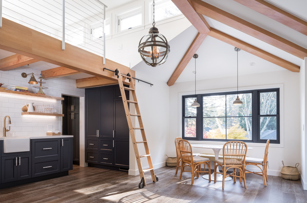 آشپزخانه‌ای مدرن با کابینت‌های سورمه‌ای، سینک سرامیکی، نردبان چوبی برای دسترسی به طبقه بالا، پنجره‌های بزرگ و سقف شیب‌دار با تیر چوبی  