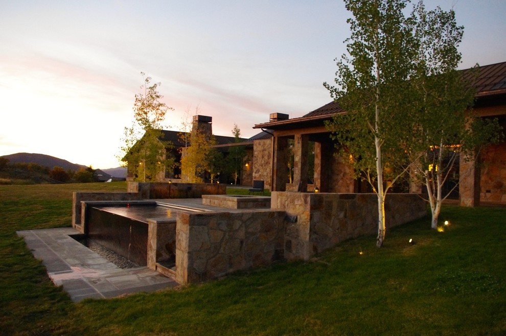 محوطه‌سازی باغ با آب‌نما سنگی، معماری طبیعی‌گرا و نورپردازی شب در طراحی ویلای مدرن با متریال بومی و منظر کوهستانی