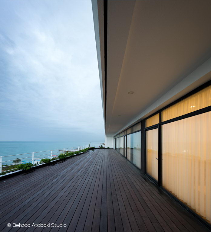 تراس چوبی ویلای مدرن با نمای شیشه‌ای سرتاسری و چشم‌انداز دریا، طراحی مینیمال در ترکیب با طبیعت ساحلی