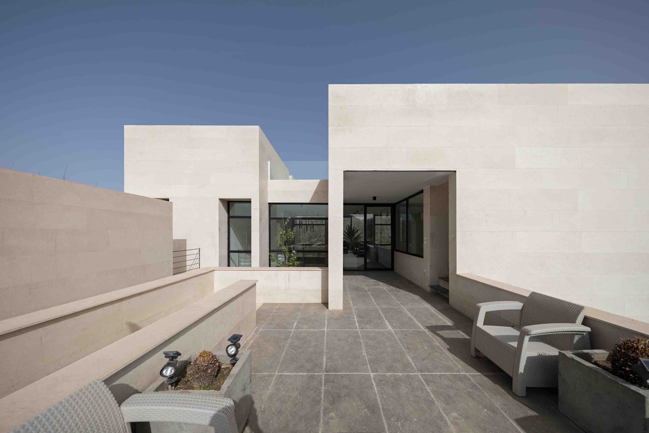 تراس ویلای مدرن با نما و کف‌پوش سنگی، طراحی مکعبی روشن و مبلمان حصیری، ترکیب خلوت و هندسی در معماری معاصر