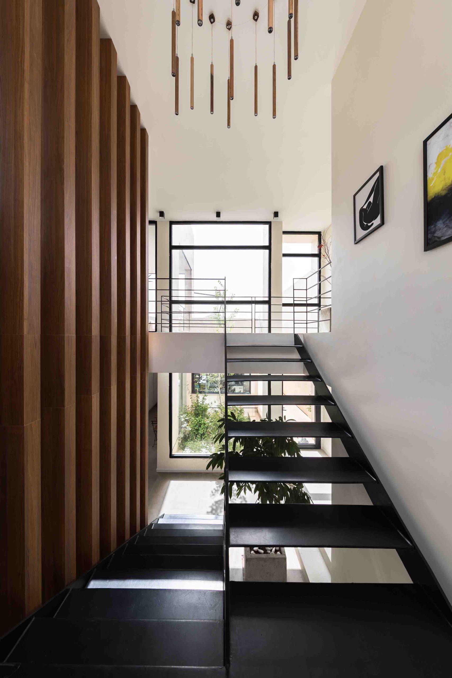 راه‌پله فلزی مشکی با دیوارکوب چوبی، پنجره قدی نورگیر و لوستر مدرن، تلفیقی از جزئیات معمارانه در طراحی داخلی ویلا