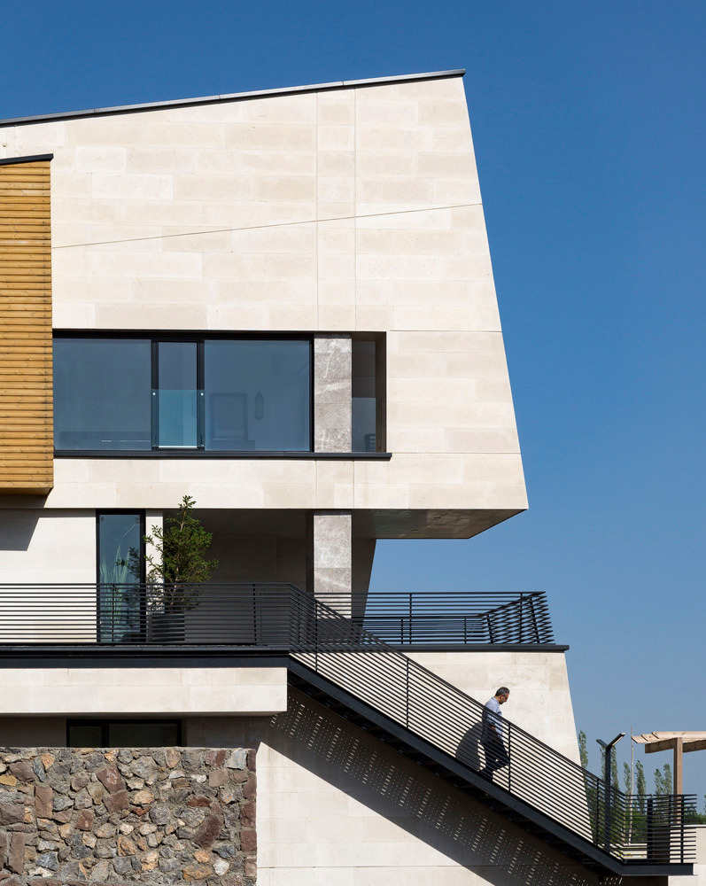 نمای جانبی ویلای مدرن با نمای سنگی روشن، خطوط تمیز، پنجره‌های مینیمال و راه‌پله فلزی مشرف به محوطه