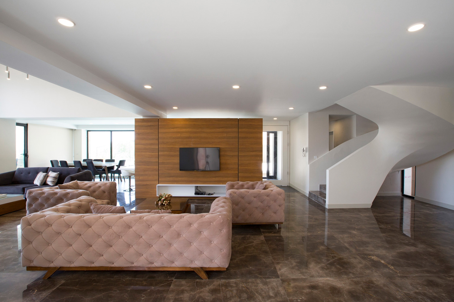 نمای داخلی ویلای مدرن با طراحی مینیمال، مبلمان کلاسیک، دیوار چوبی تلویزیون و راه‌پله منحنی سفید