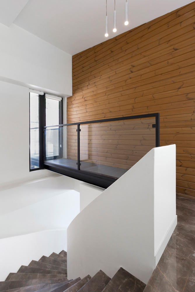 راه‌پله داخلی ویلای مدرن با دیوار سفید منحنی، کف سنگی، نورپردازی مینیمال و دیوارکوب چوبی عمودی